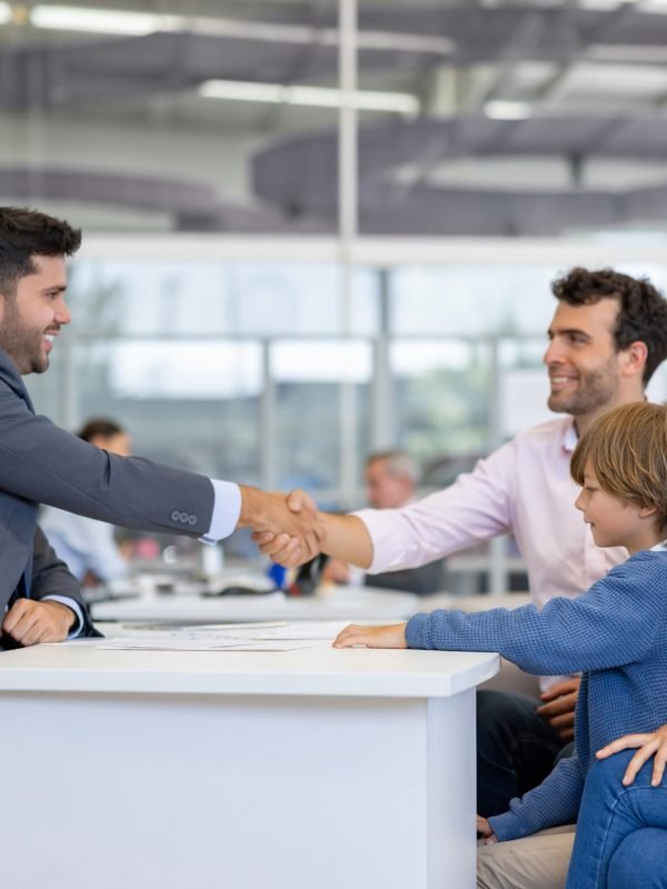 Happy Latin American family closing a deal with a salesman and handshaking while buying a car at the dealership